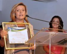 Aparecida Benito Pereira pronunciando, emocionada, sobre o prêmio recebido.
Ao Fundo Mira Graçano, reporter e apresentadora da RPC TV, afiliada da Rede Globo.